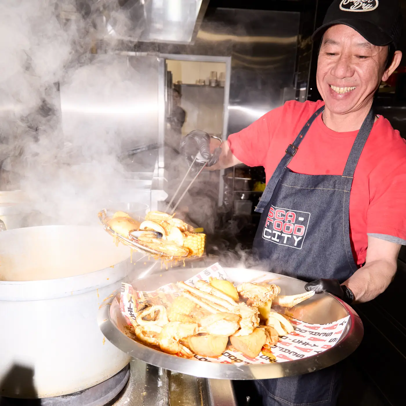 Seafood City Birmingham chef in the kitchen preparing a Louisiana-style seafood boil — handling fresh King prawns, lobster and Cajun-spiced broth